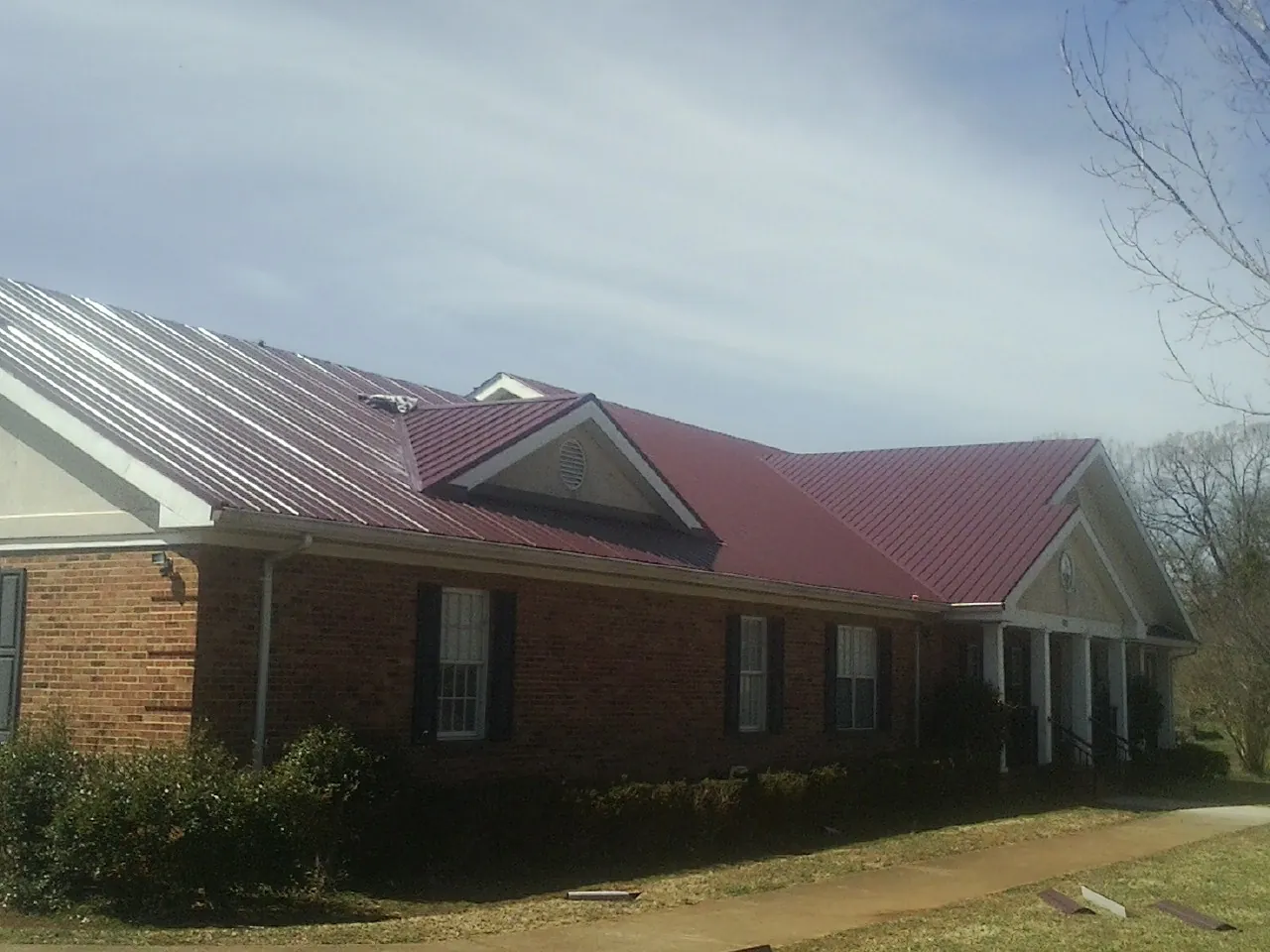 Red metal roof with gabled entries on a long brick building, from a Hail Damage Roof Repair job in Marietta